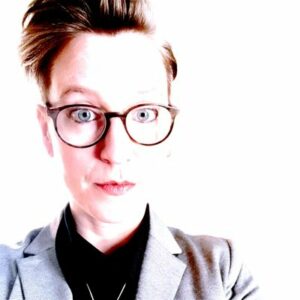 white woman with reddish hair, blue eyes, and glasses looks directly at the camera